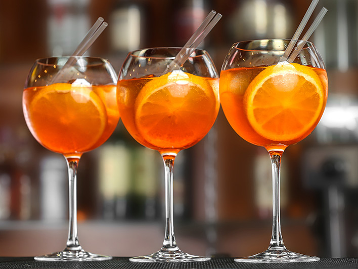 Three orange cocktail drinks on the bar with straws and a slice of orange
