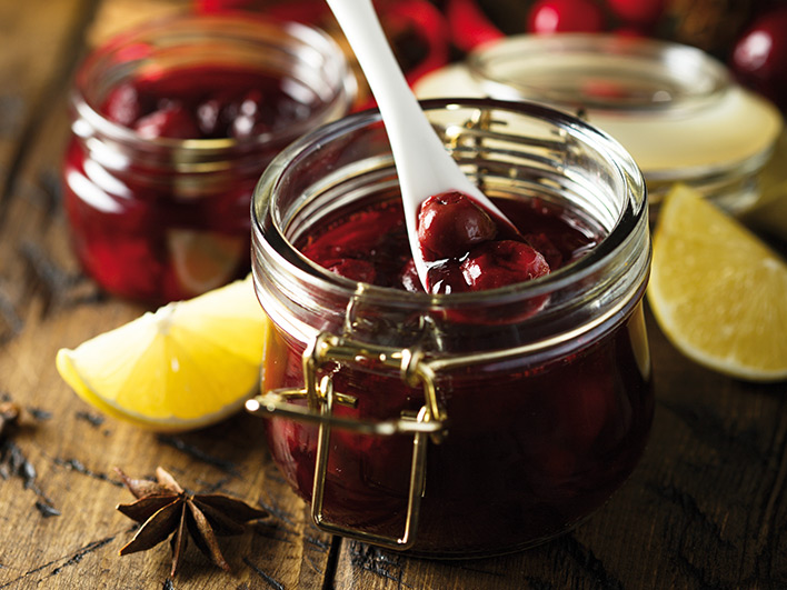 A jar of cranberry sauce with wedges of lemon and a spoon