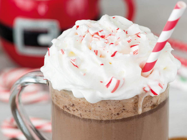 A mug of peppermint chocolate topped with cream with a red striped straw